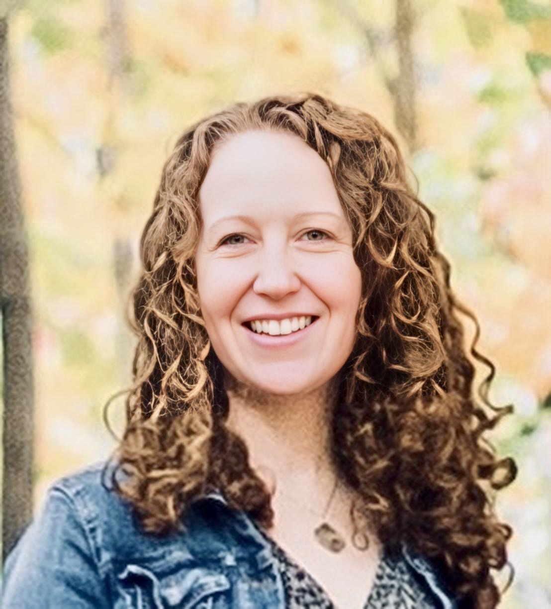 a headshot of a woman with red curly hair smiling wearing a jean jacket