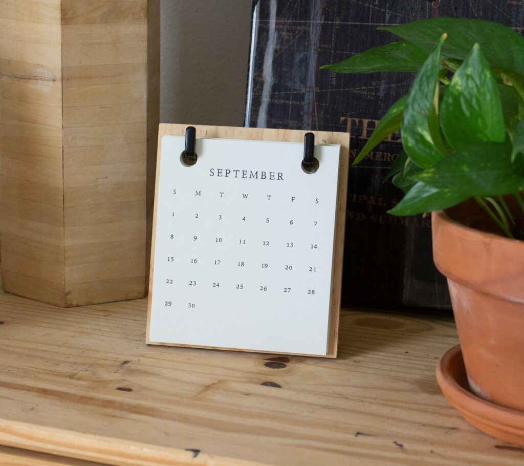 September calendar on a wooden shelf with a green Ivy in a terracotta container.