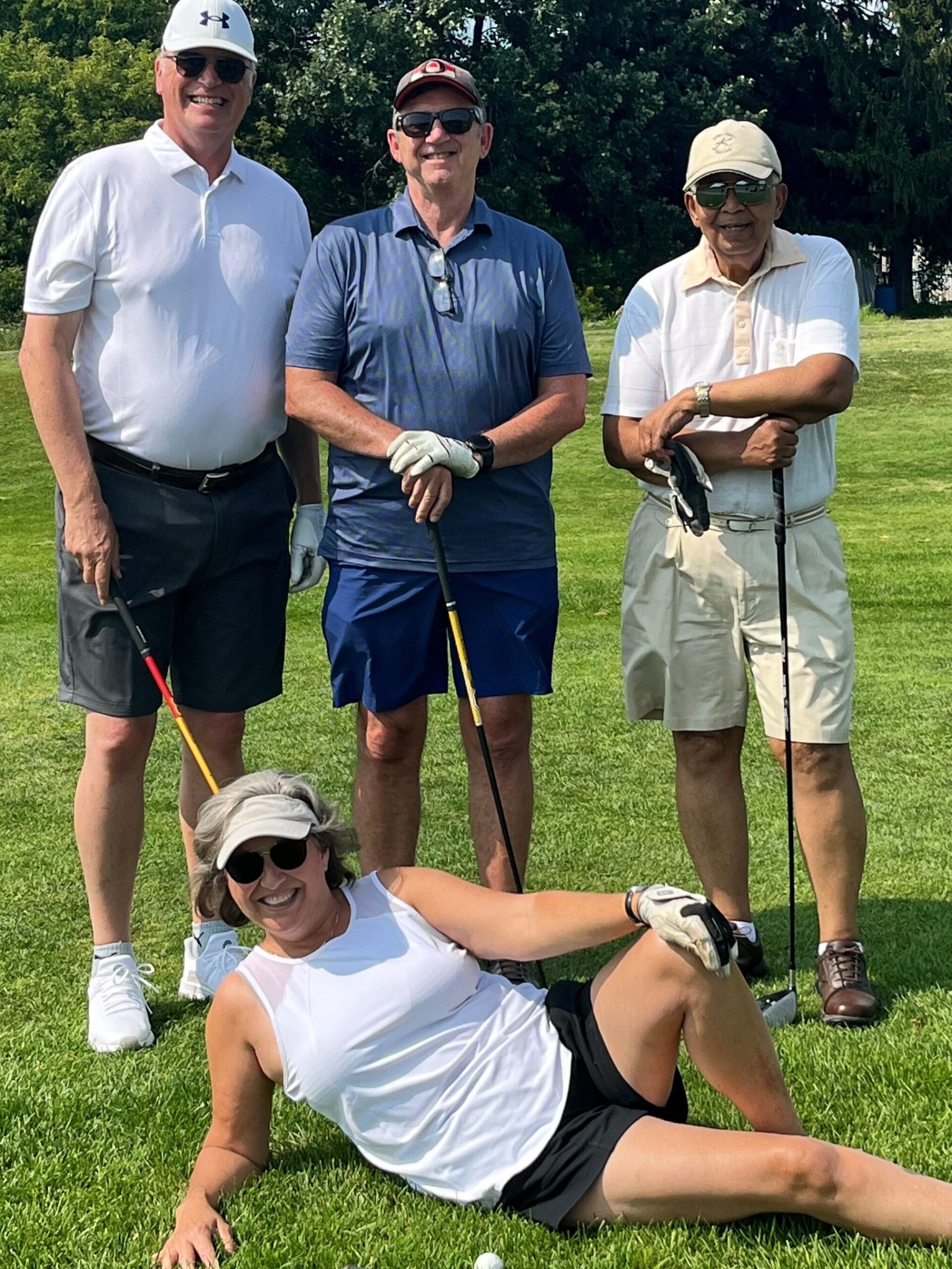 a team of three men standing with one woman reclining at the start of a golf tournament