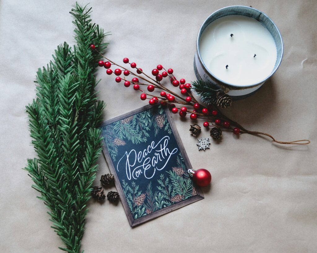 Christmas card with 'Peace on Earth' on the front surrounded by a pine branch, a branch with berries, pinecones, a red Christmas ornament and a candle