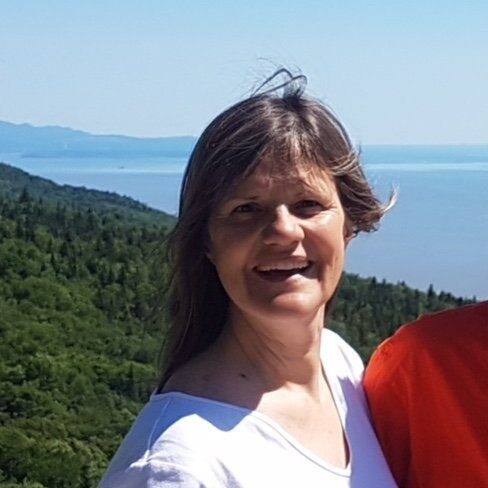 a smiling woman with shoulder length brown hair wearing a white top