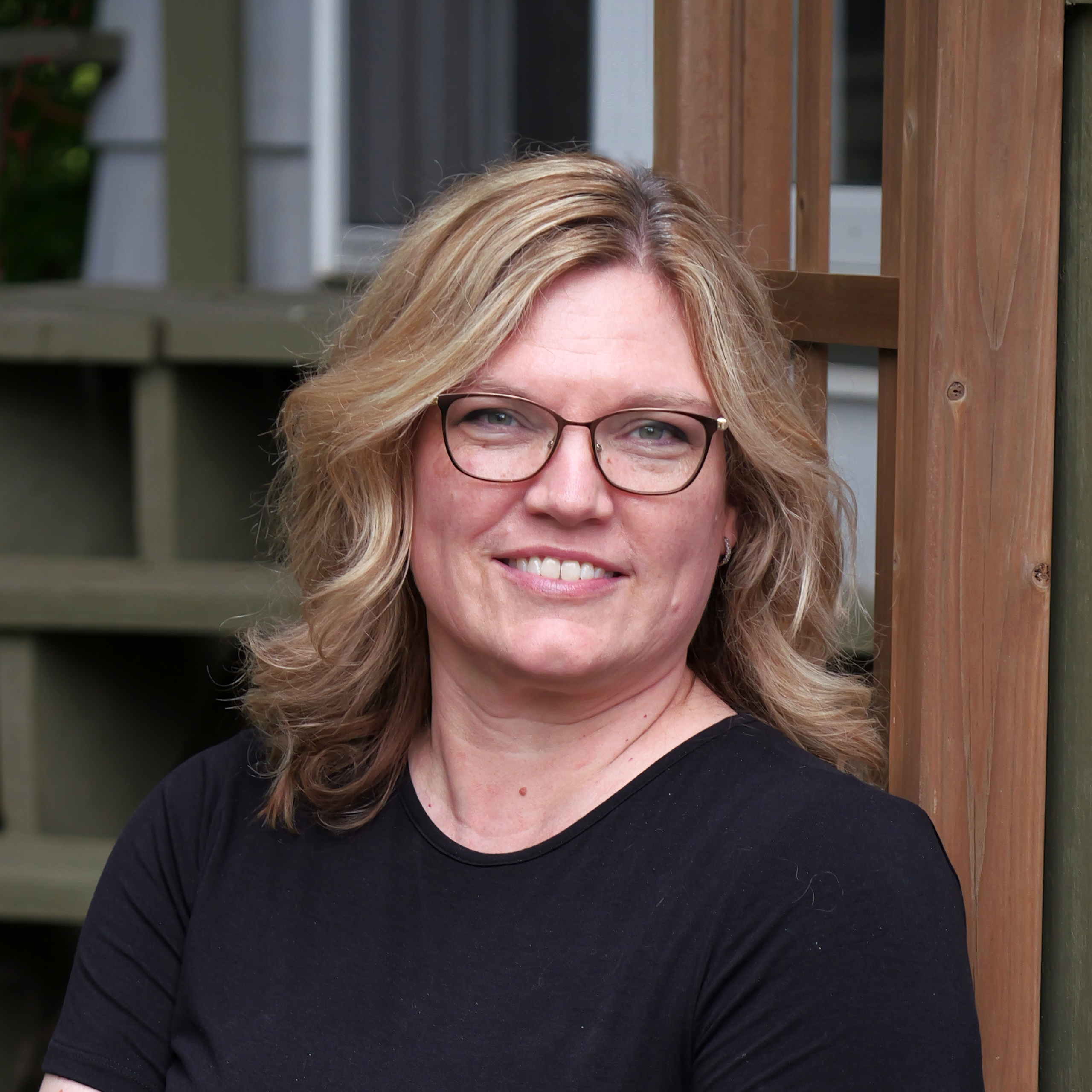 a headshot of a smiling woman with glasses and shoulder length light brown hair wearing a black top