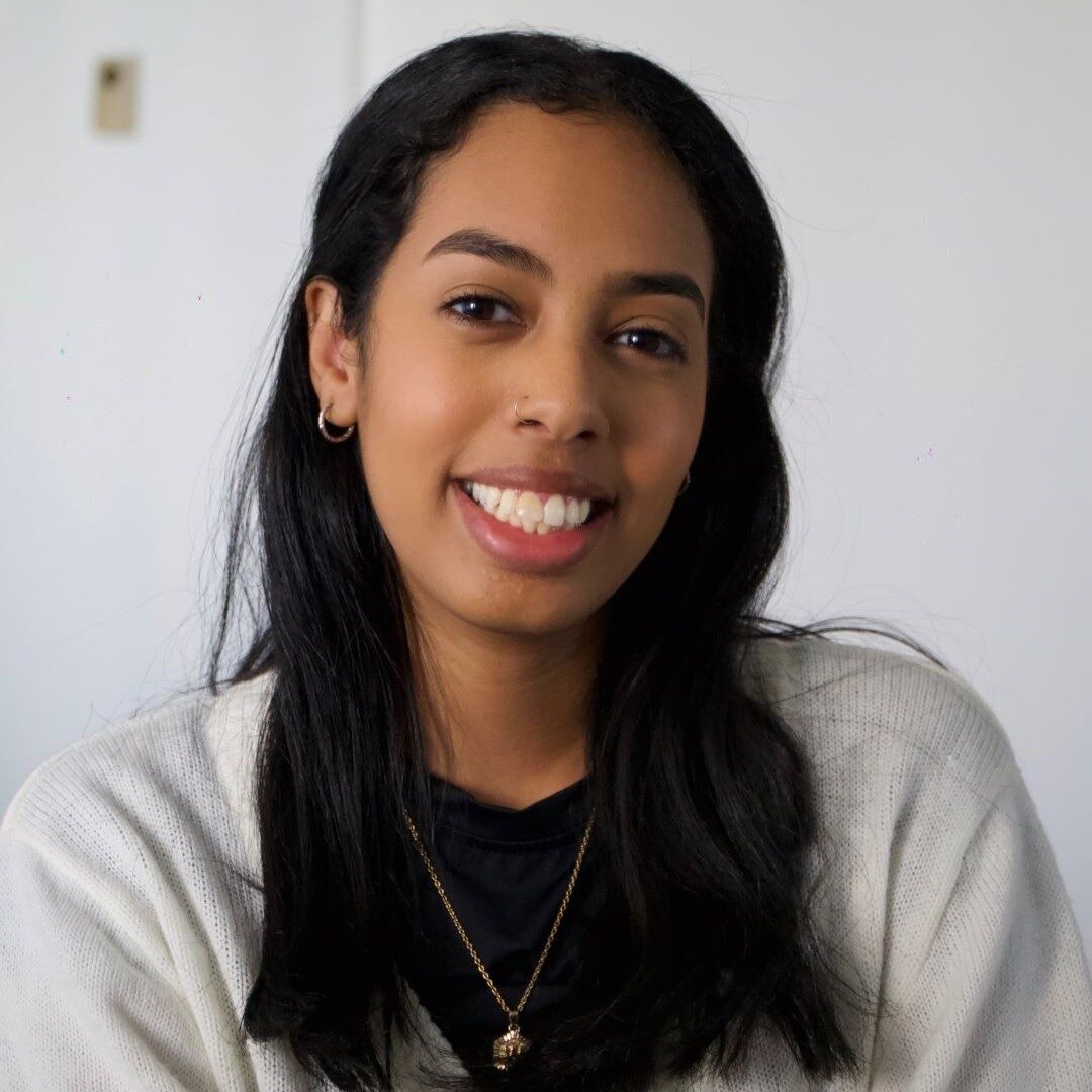 a headshot of a smiling woman with long dark hair wearing a white sweater