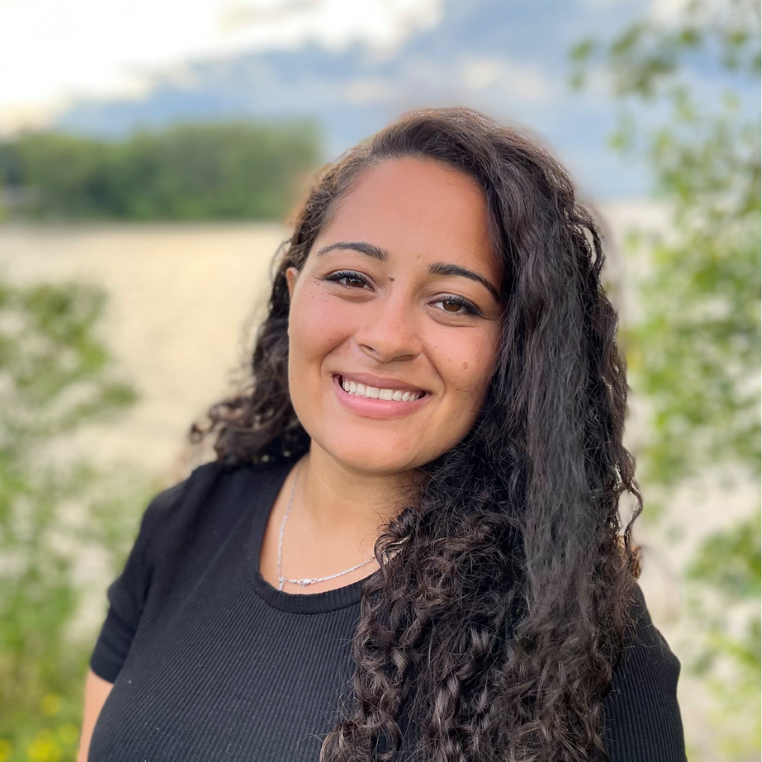 a smiling woman with long curly dark brown hair wearing a black top