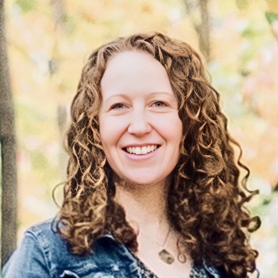 a headshot of a woman with red curly hair smiling wearing a jean jacket