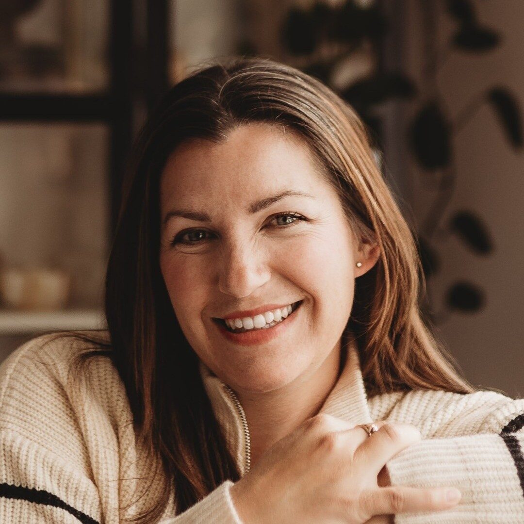 a headshot of a smiling woman with long brown hair wearing an ivory sweater with black stripe